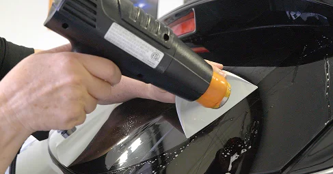 Close-up of a person using a heat gun and squeegee to apply and smooth window tint film on the rear windshield of a car.