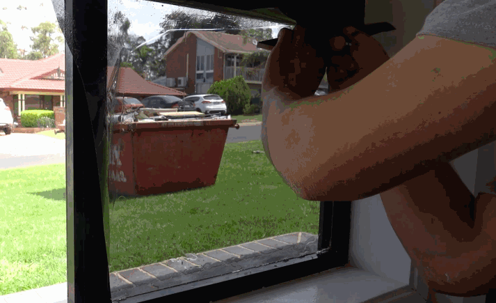 Installer applying residential window tinting film to a small window using a squeegee for a smooth finish.