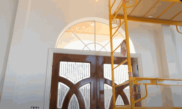 Tall entryway with decorative double doors and upper windows being prepped for home window tint installation using scaffolding for high access.