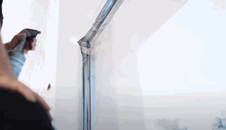 Close-up of a technician spraying solution and smoothing a sheet of window tint onto a commercial glass surface during the installation process.