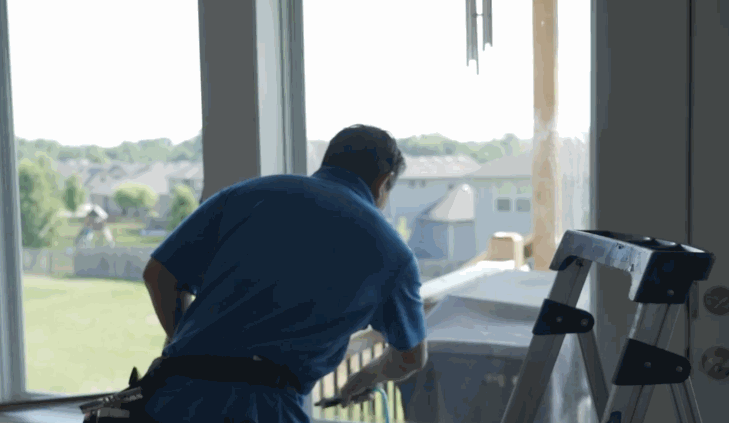 The same technician smooths out a newly installed home window film on glass patio doors using a blue squeegee tool, ensuring no bubbles remain.