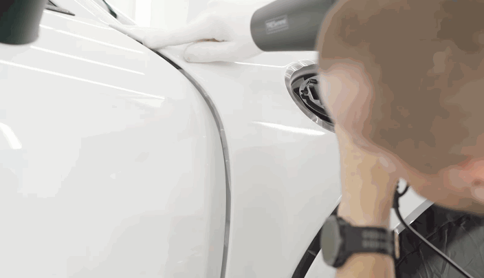 A close-up view of a technician using a heat gun to secure paint protection film along a car’s fender edge.