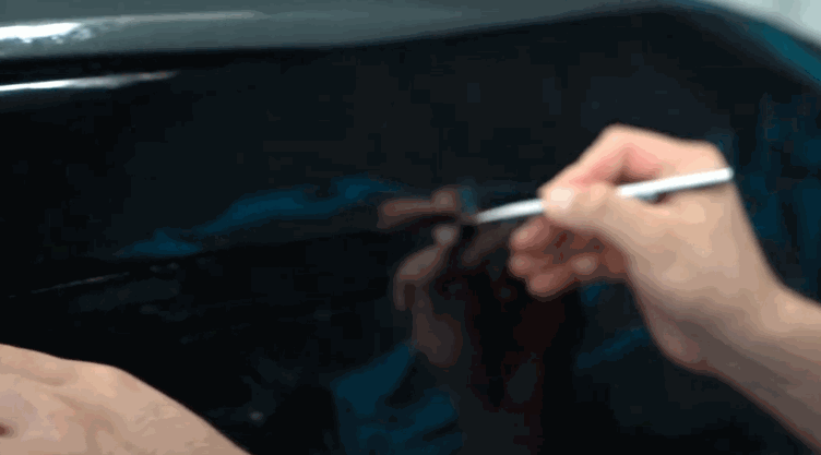 A close-up of a person trimming excess tint film with a precision knife along the edge of a car window.
