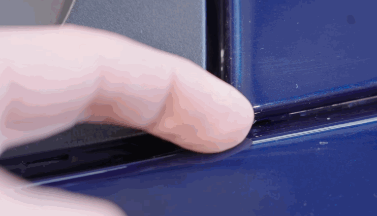 A finger gently presses the edge of a car panel to check the seamless installation of paint protection film.
