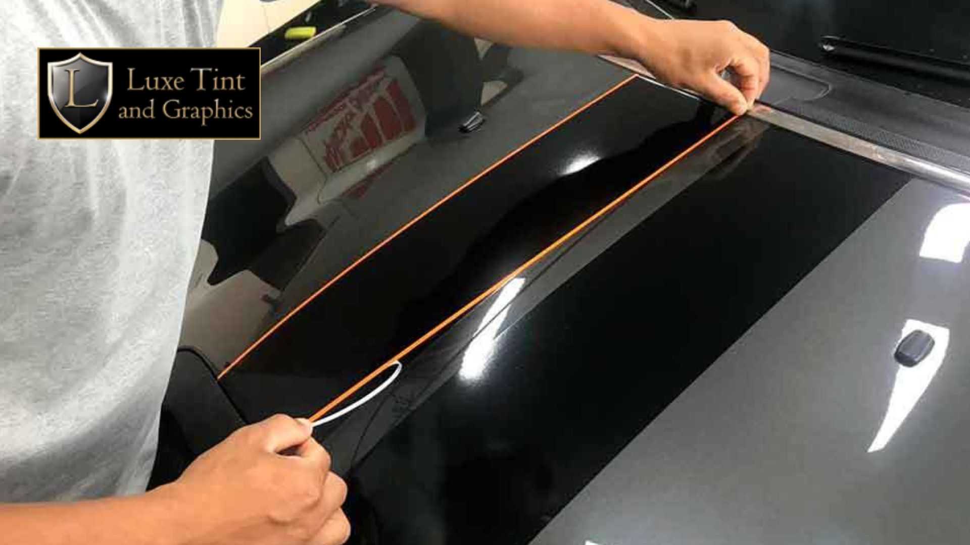 Person applying precision vinyl pinstripes on a black car hood as part of a custom paint protection film service at Luxe Tint and Graphics.