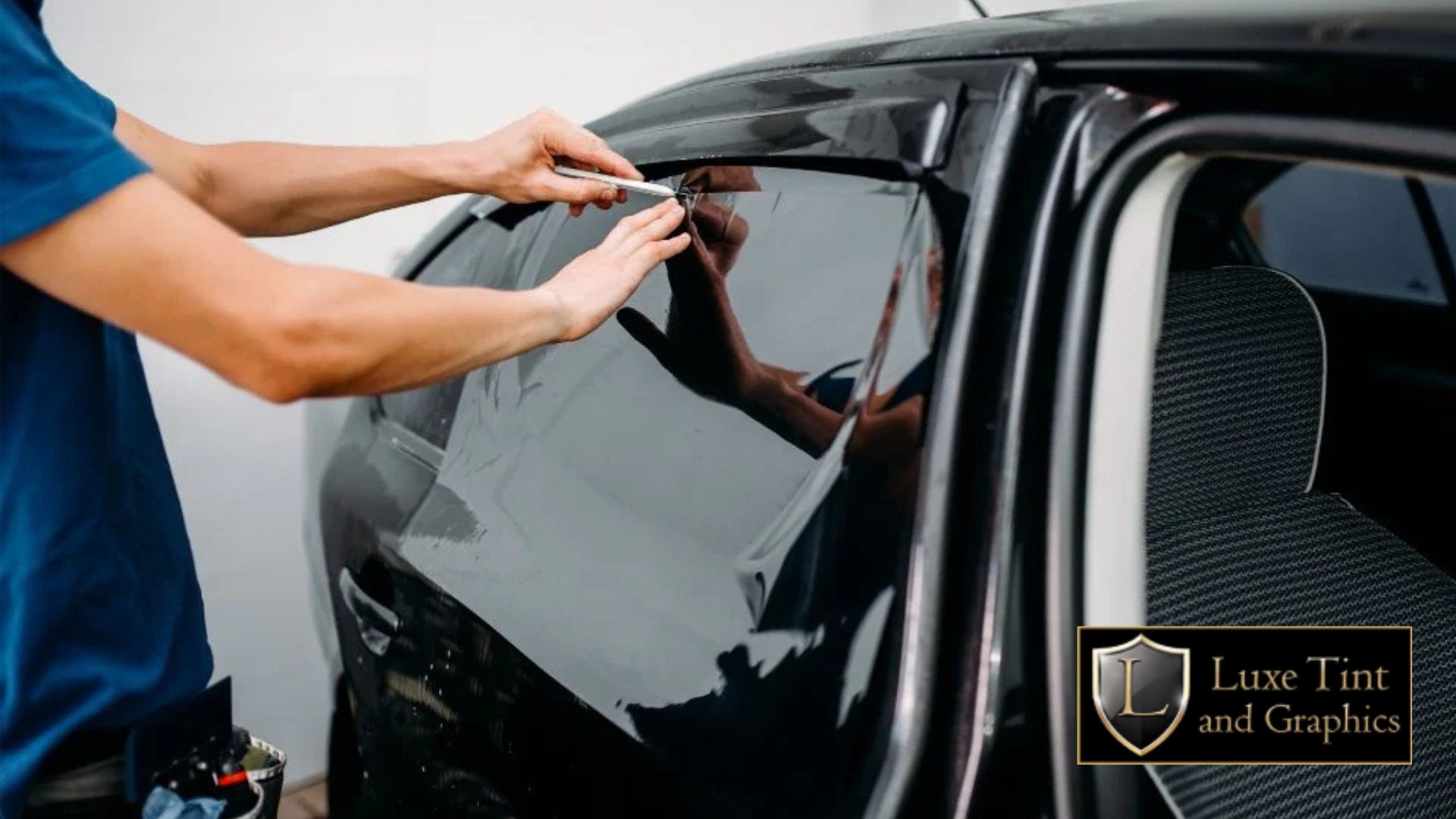 Close-up of a technician carefully trimming excess window tint film on a car’s rear side window using a precision blade. The film appears fully applied and reflective.